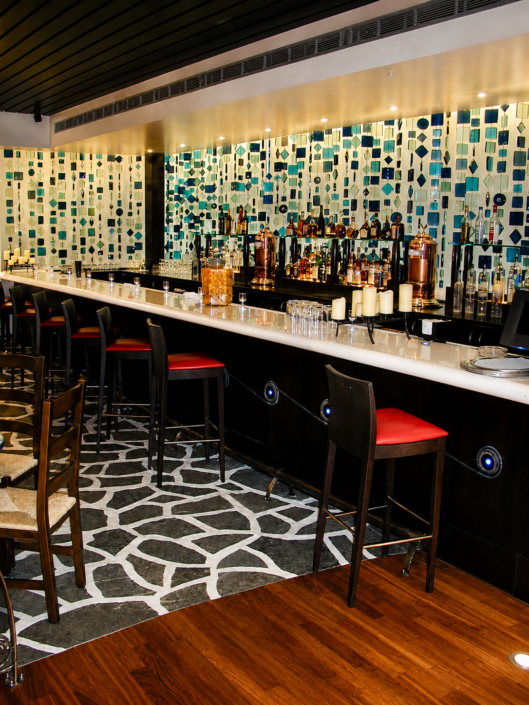 Modern bar interior with tiled wall, counter stools, and patterned carpet under warm lighting