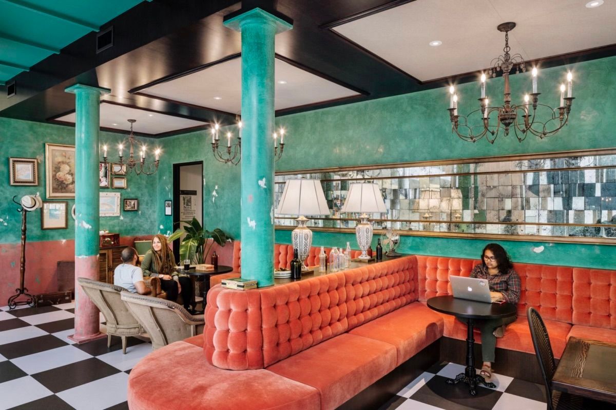 Interior of a cafe with a long orange velvet booth, turquoise columns, and black and white checkered floor.