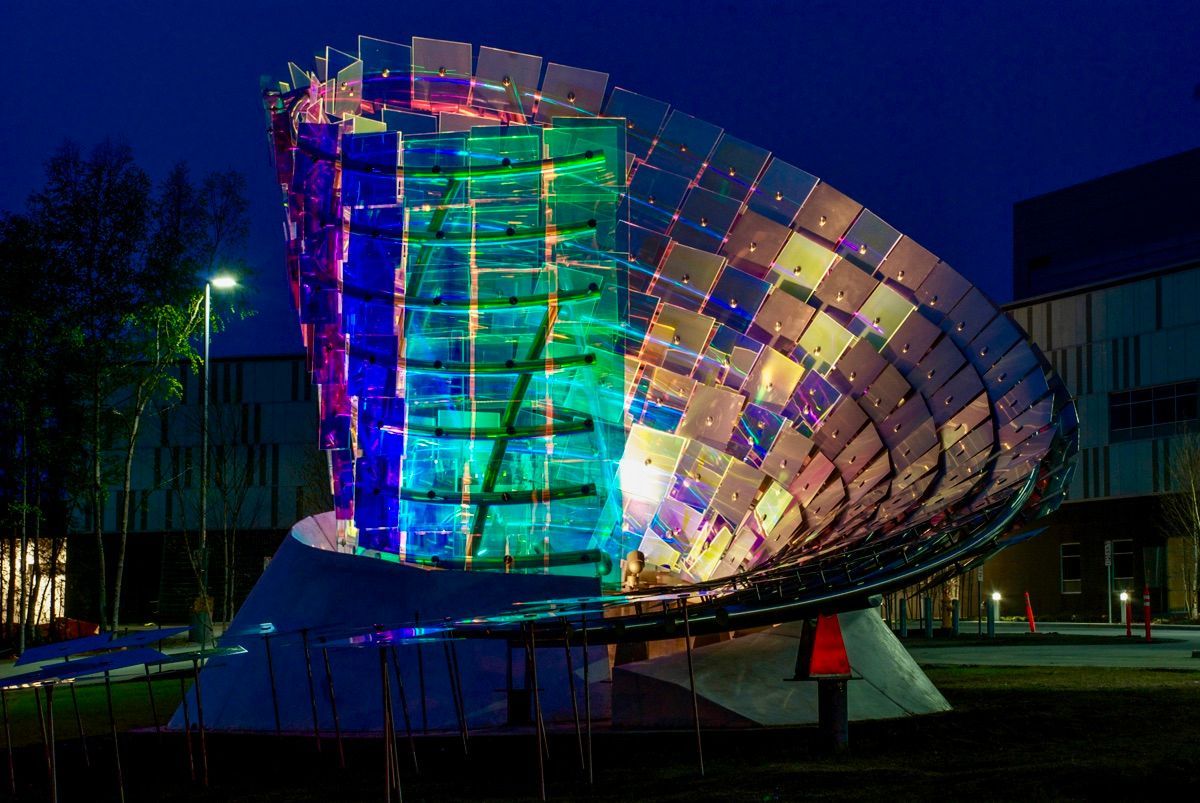Colorful illuminated modern glass building at night with a curved, shell-like facade