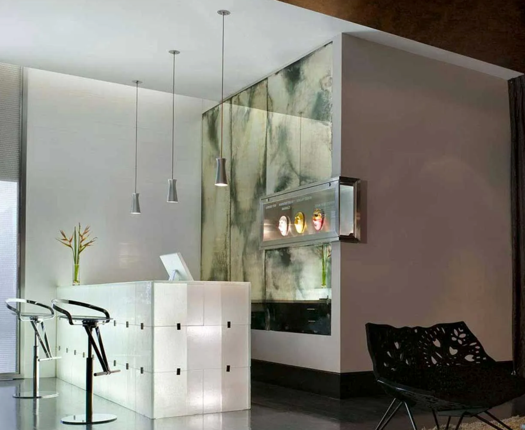 Modern lobby with white desk, hanging lights, glass wall, and black chair
