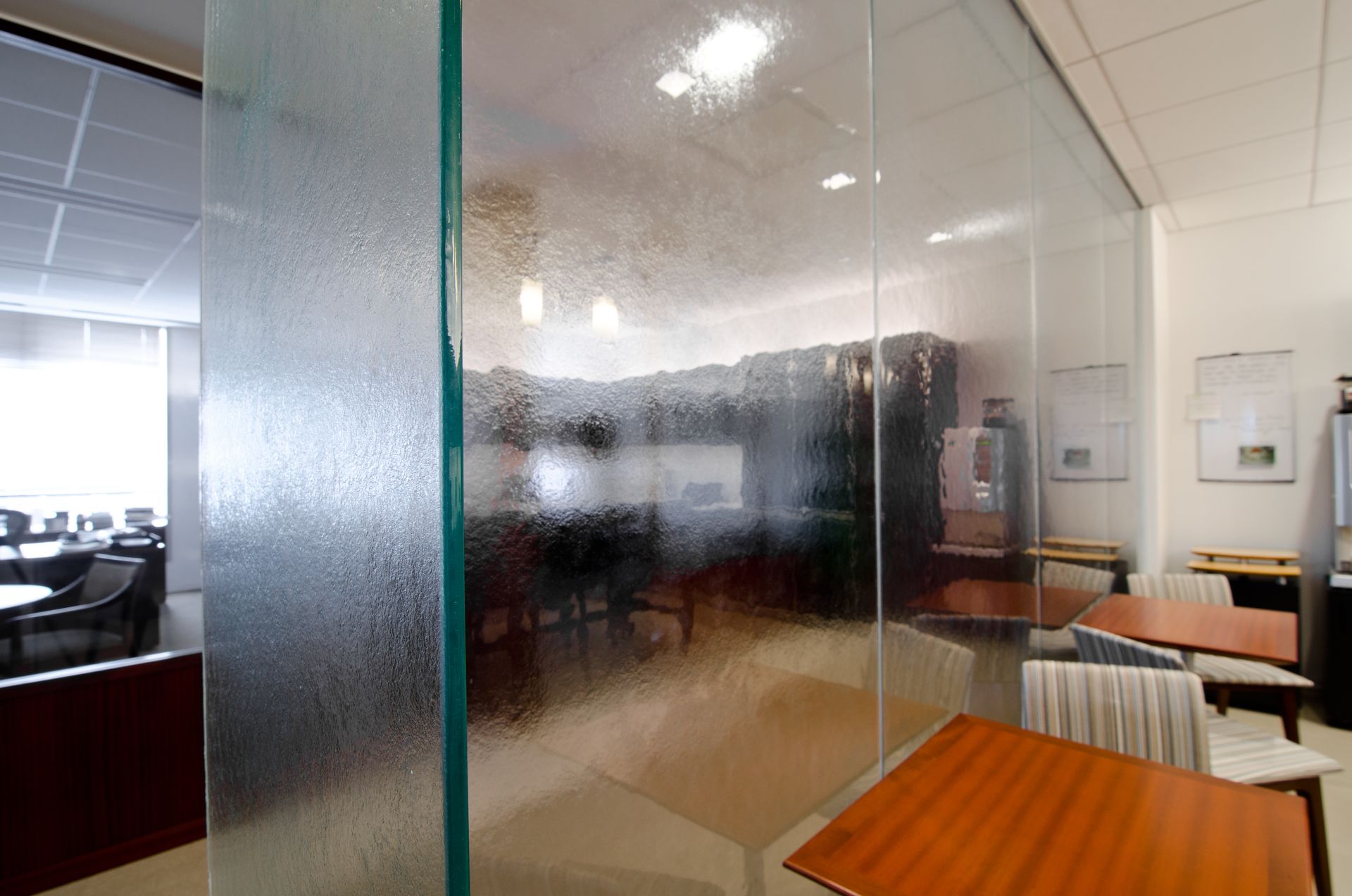 Glass-walled office meeting room with table, chairs, and frosted privacy panel
