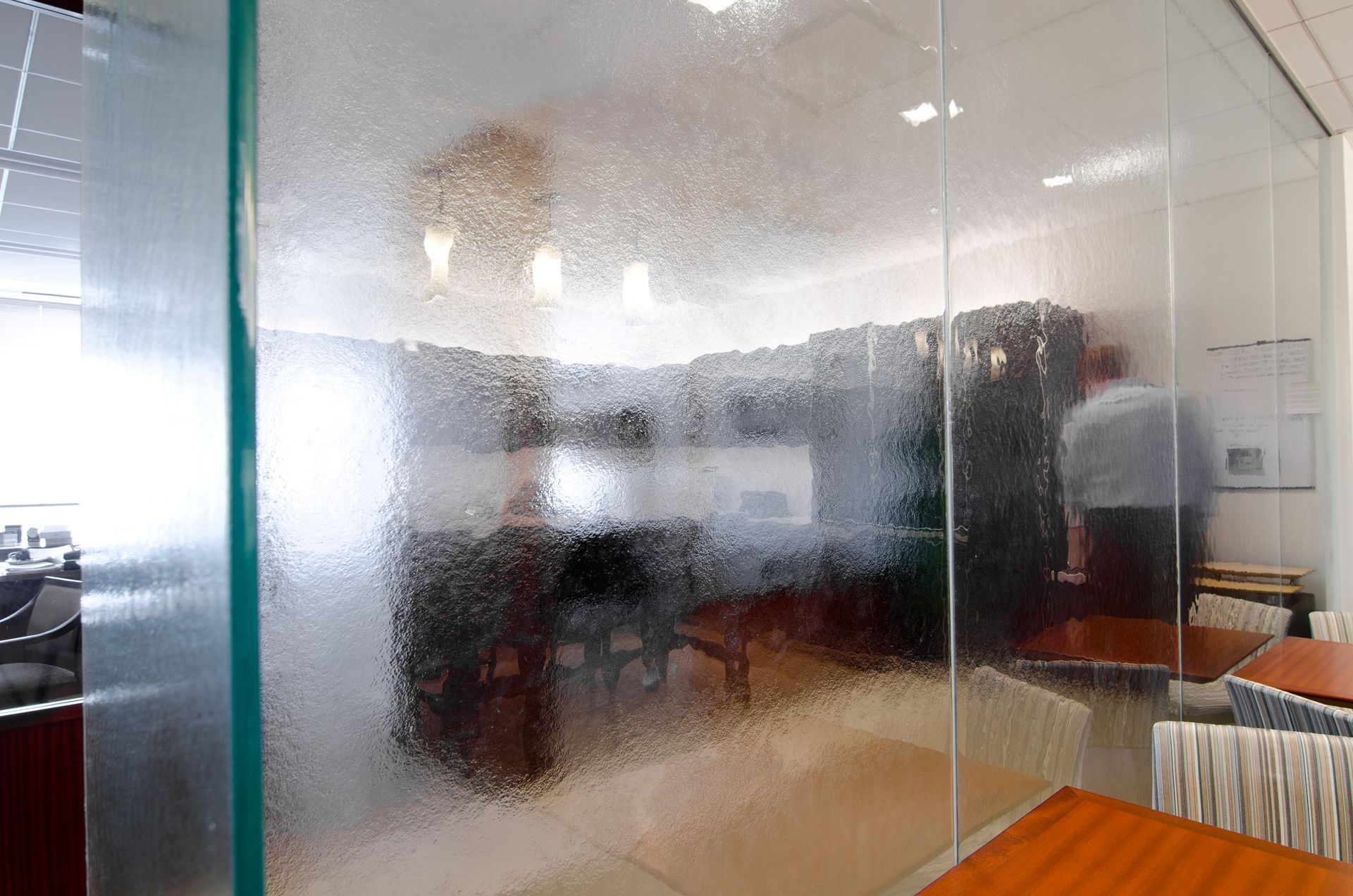 Frosted glass office partition with blurred desks and chairs in a bright workspace