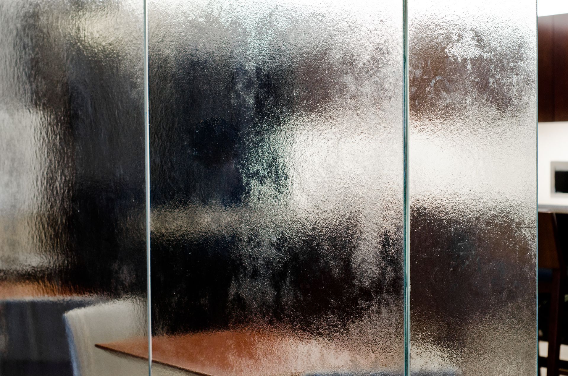 Frosted glass partition with blurred office interior behind it, including a desk and chair