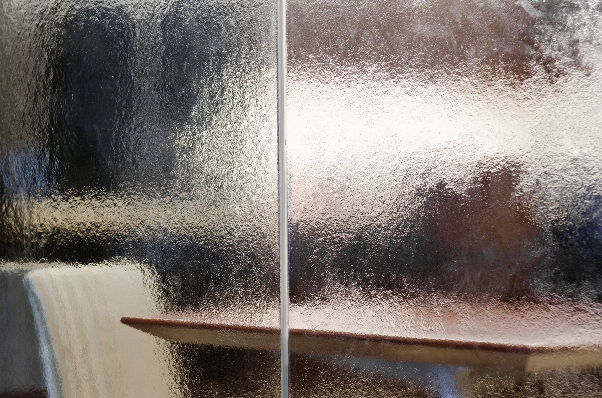 Frosted glass window with blurred outdoor reflections and a wooden table inside near a chair