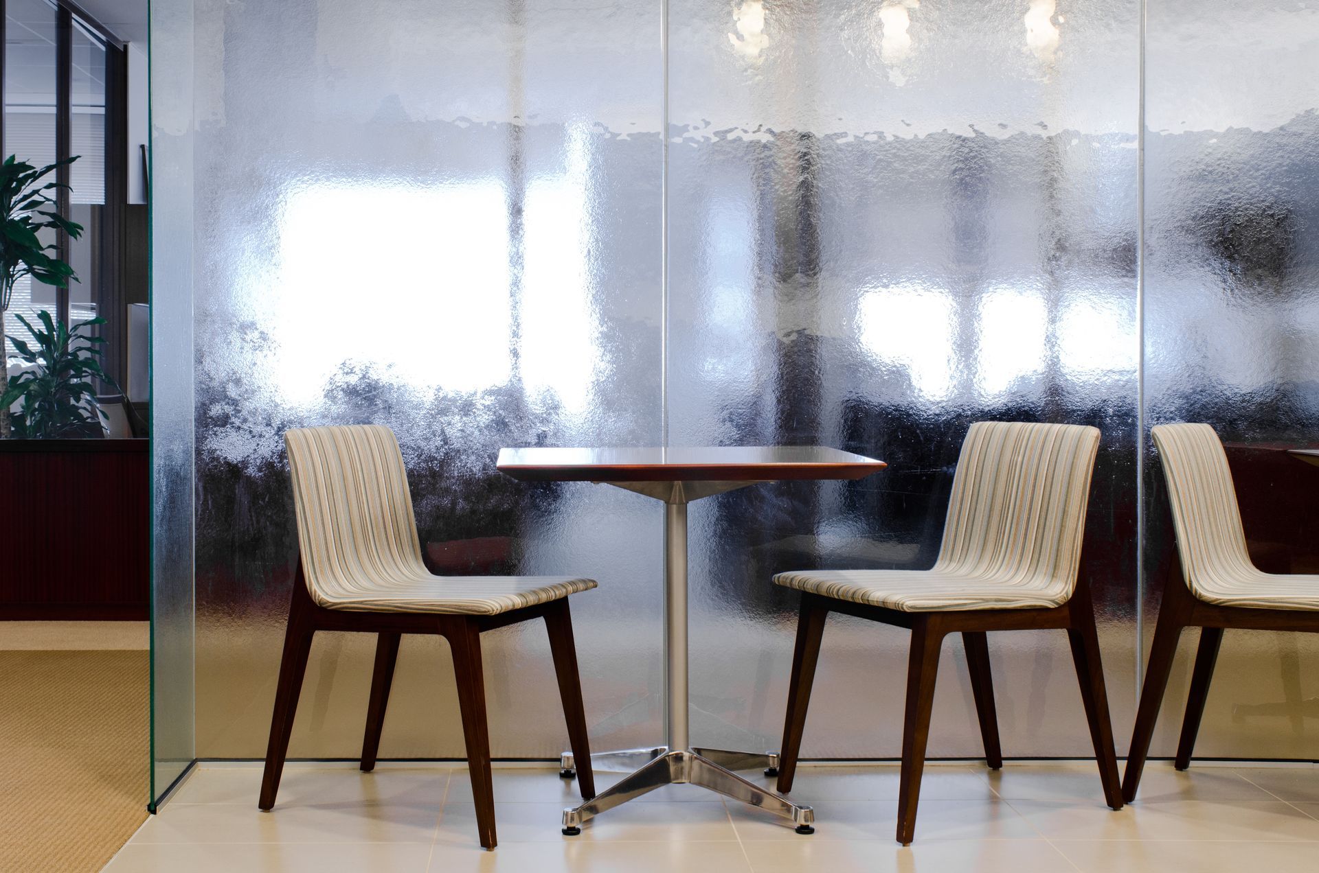 Modern café seating with two beige chairs and a small round table in front of a frosted glass wall