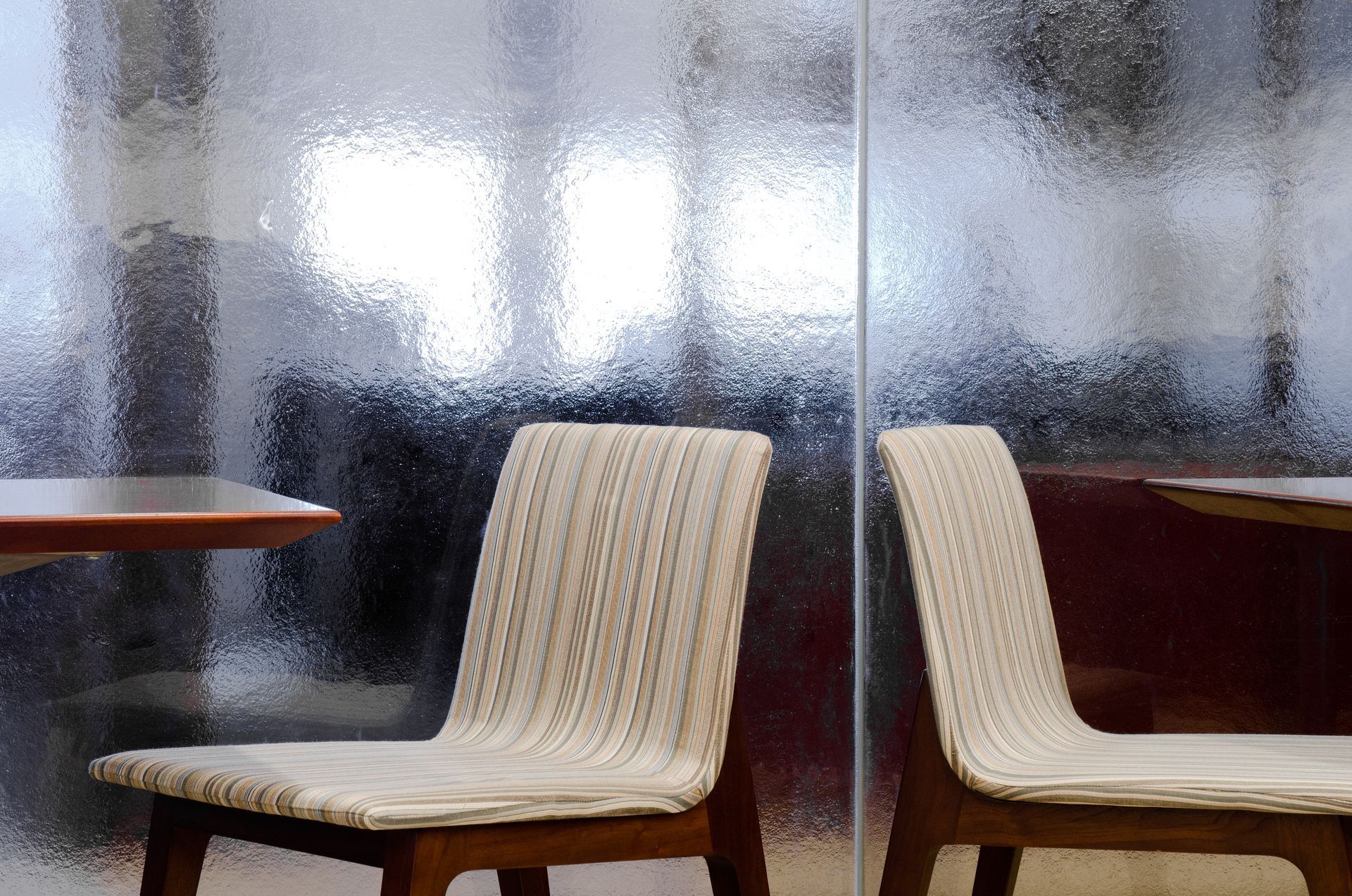 Two cream-colored chairs beside a table in a softly lit room with frosted glass walls