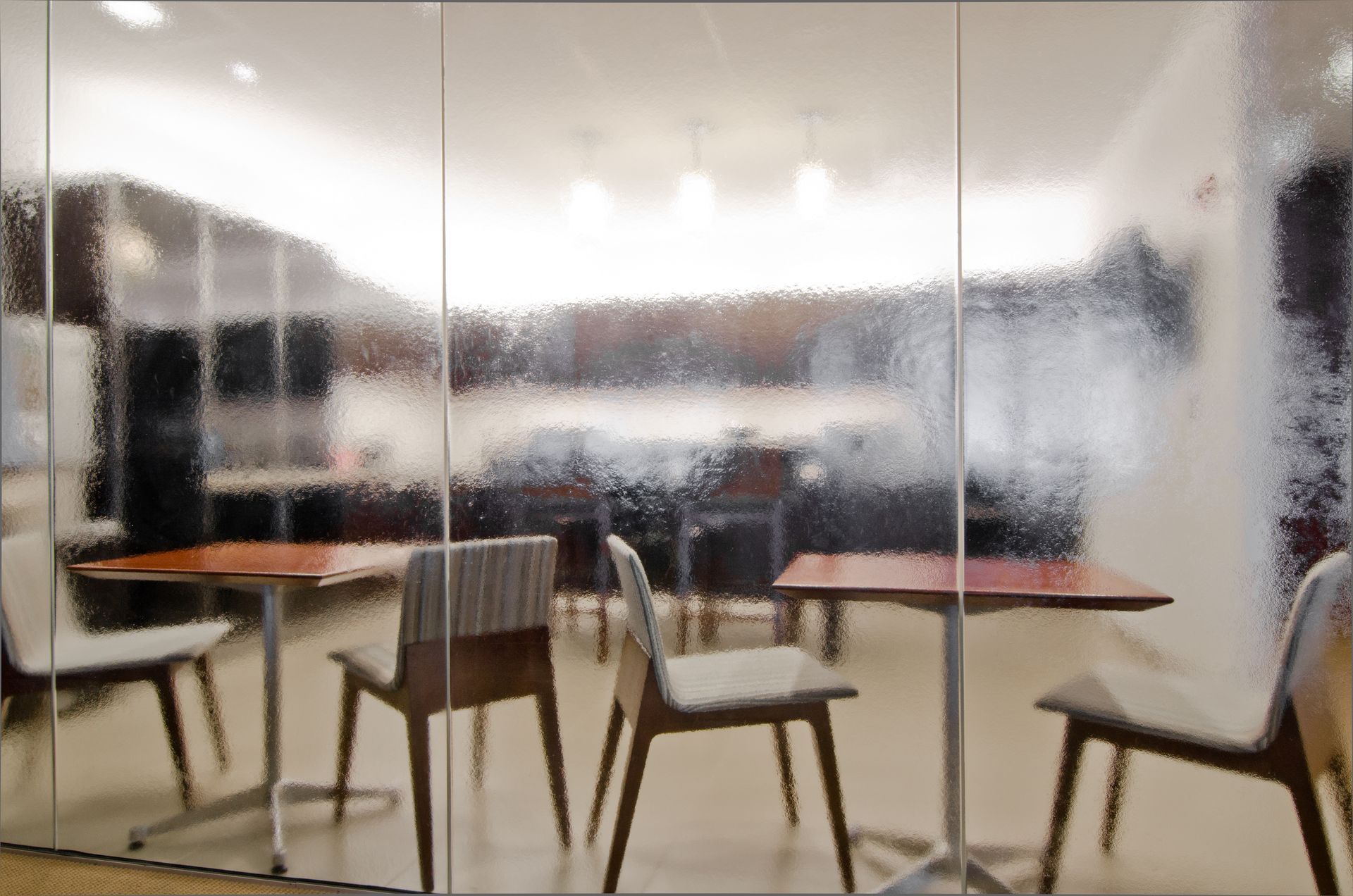 Blurred café interior with wooden chairs and tables behind frosted glass partitions.