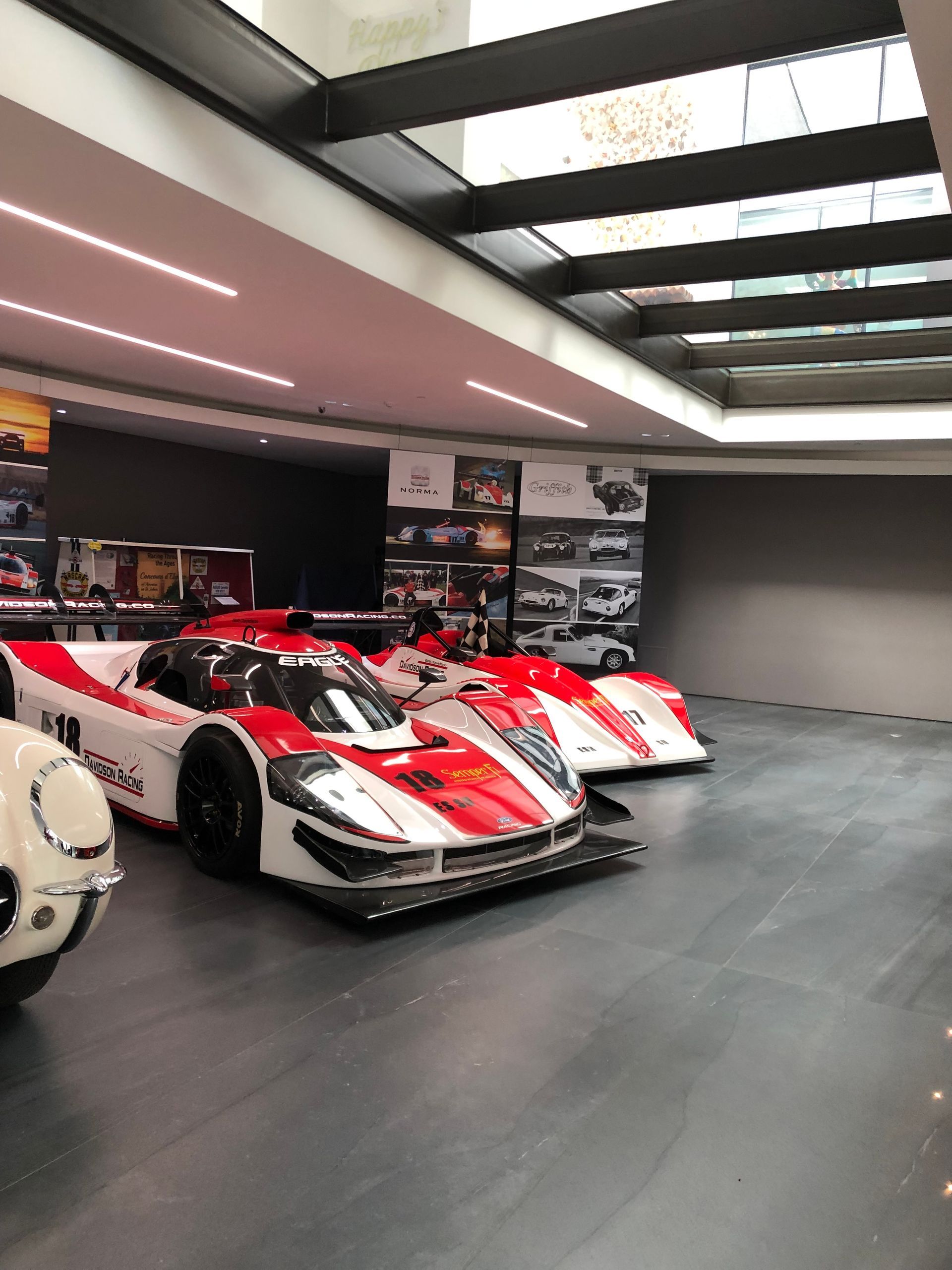 Two red-and-white race cars displayed in a modern showroom with overhead strip lighting