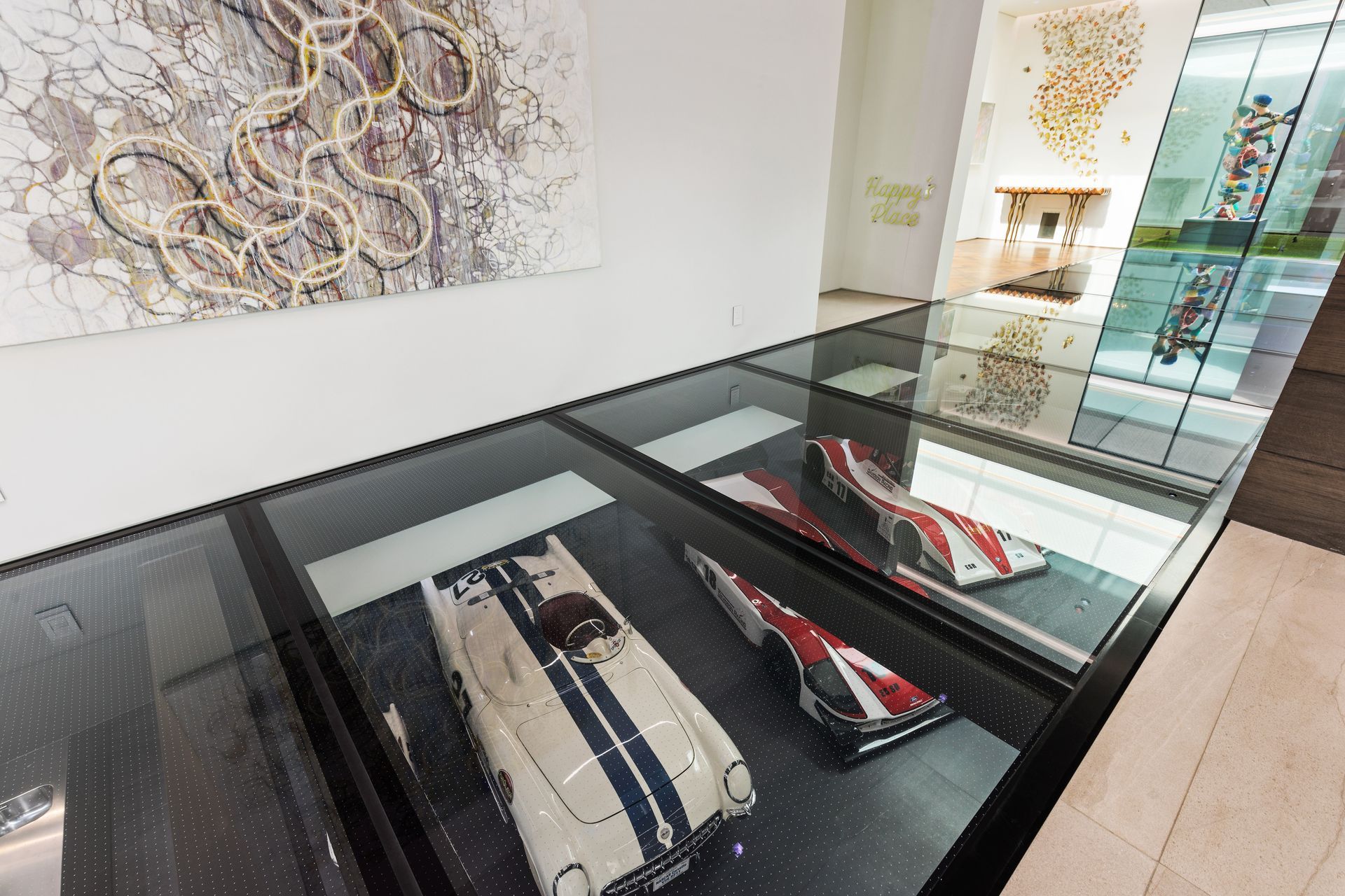 Museum display of classic race cars in glass floor cases beside an abstract wall artwork