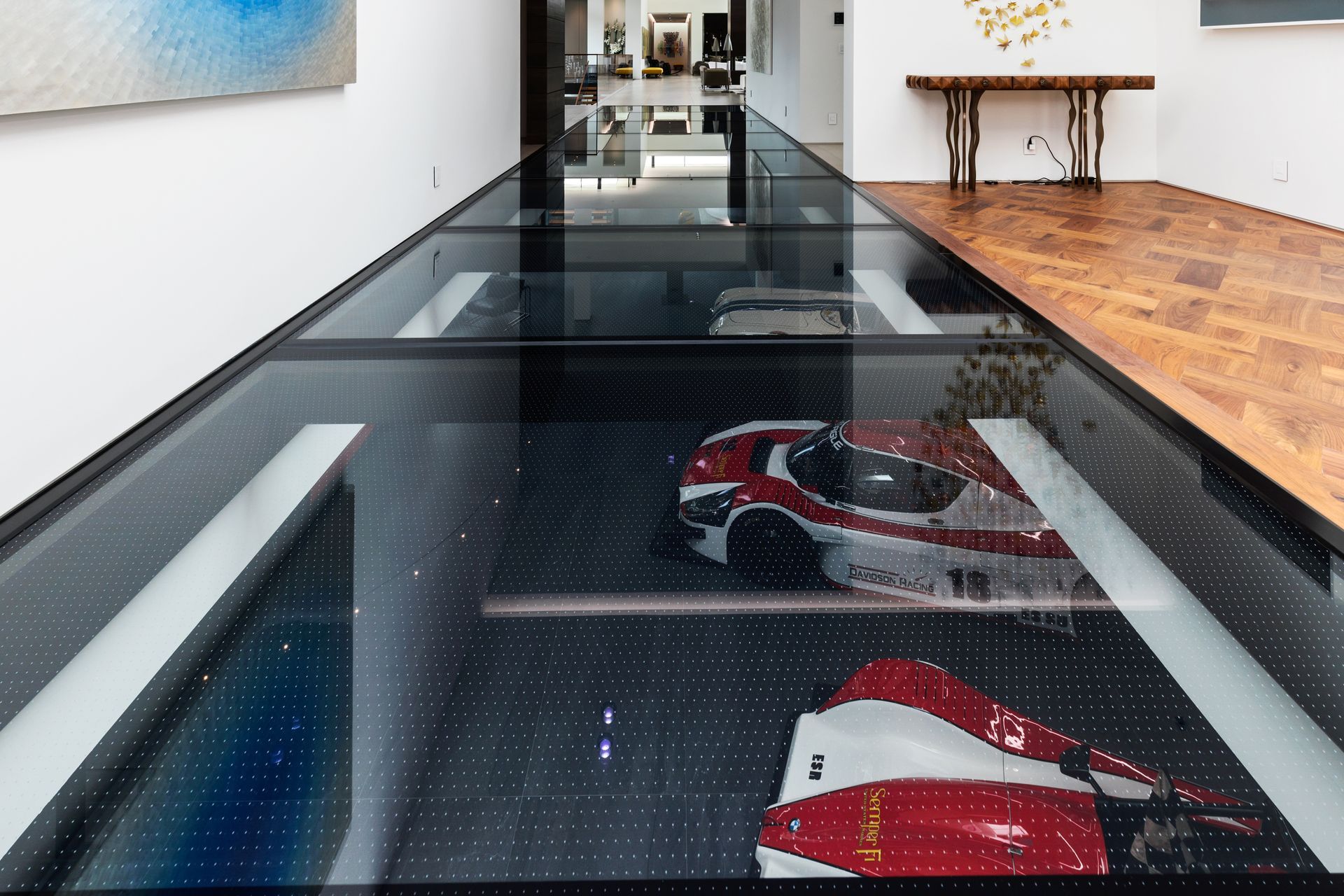 Glass floor hallway with exposed red-and-white sports cars beneath it in a modern interior