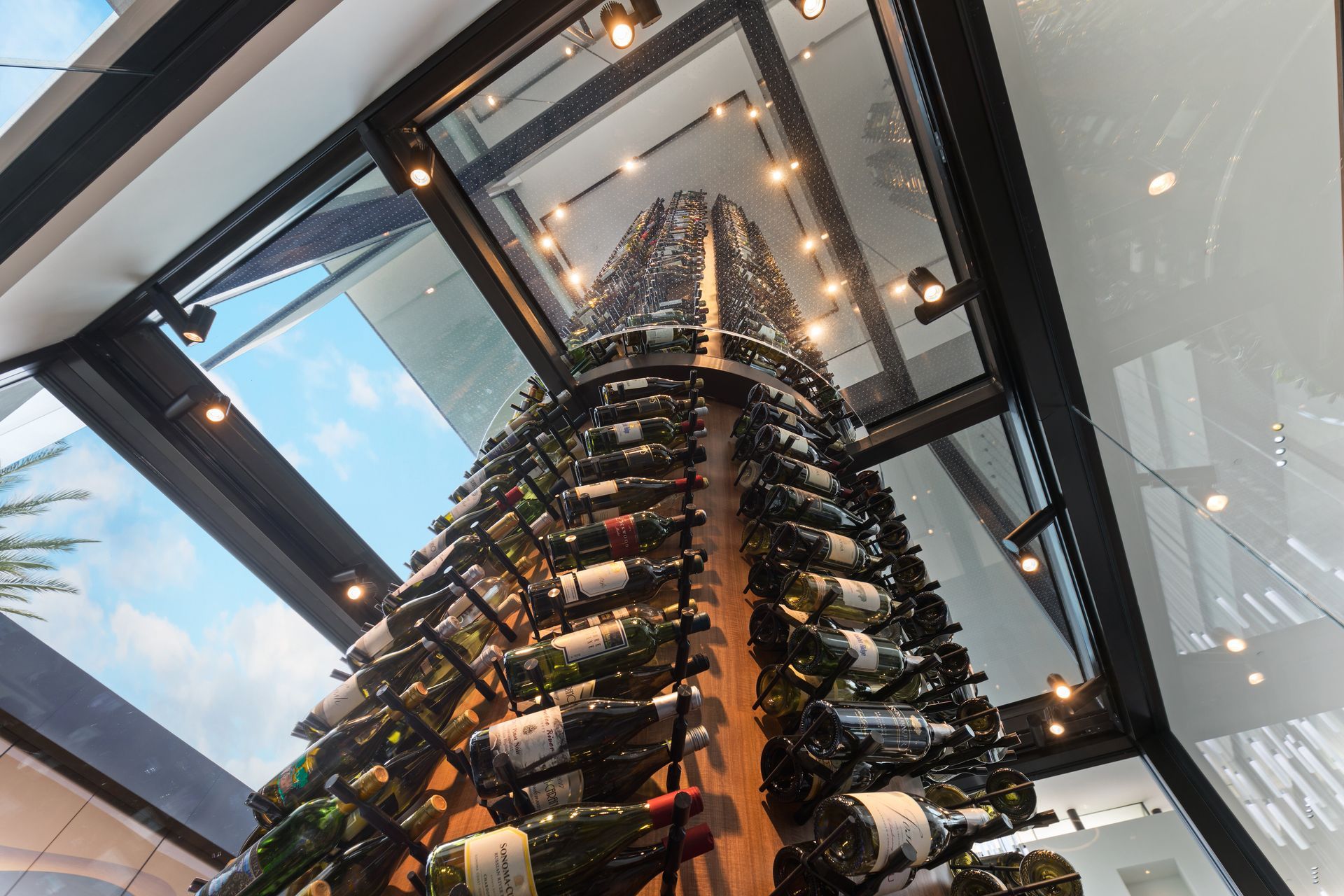 Tall wine display under a glass ceiling in a modern interior, viewed from below
