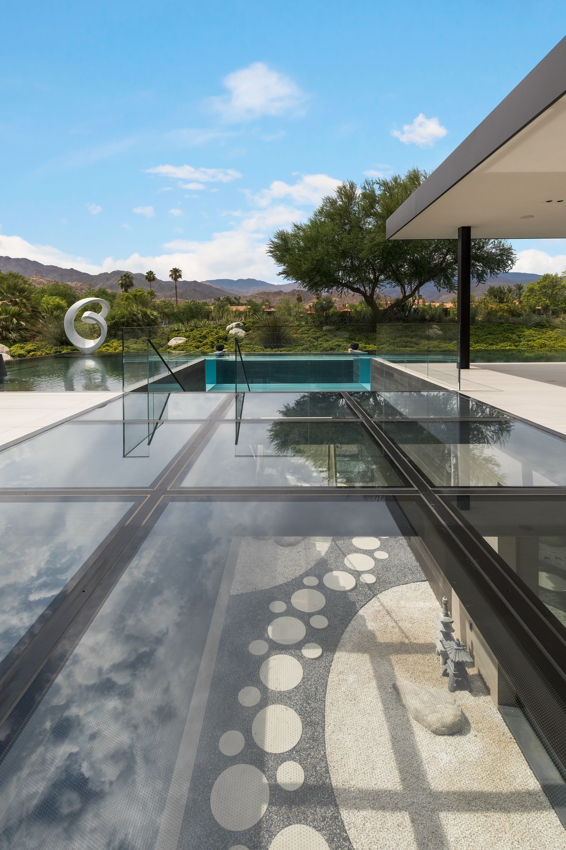 Modern patio with glass railing, turquoise pool, and desert mountains under a clear blue sky