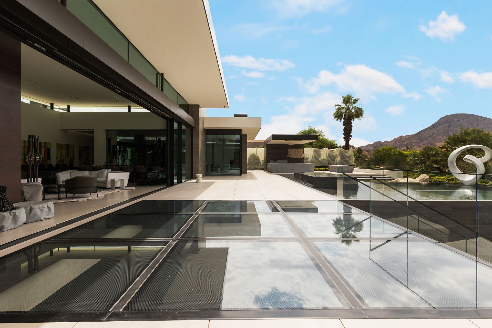 Modern house patio with glass pool reflecting a palm tree and desert mountains