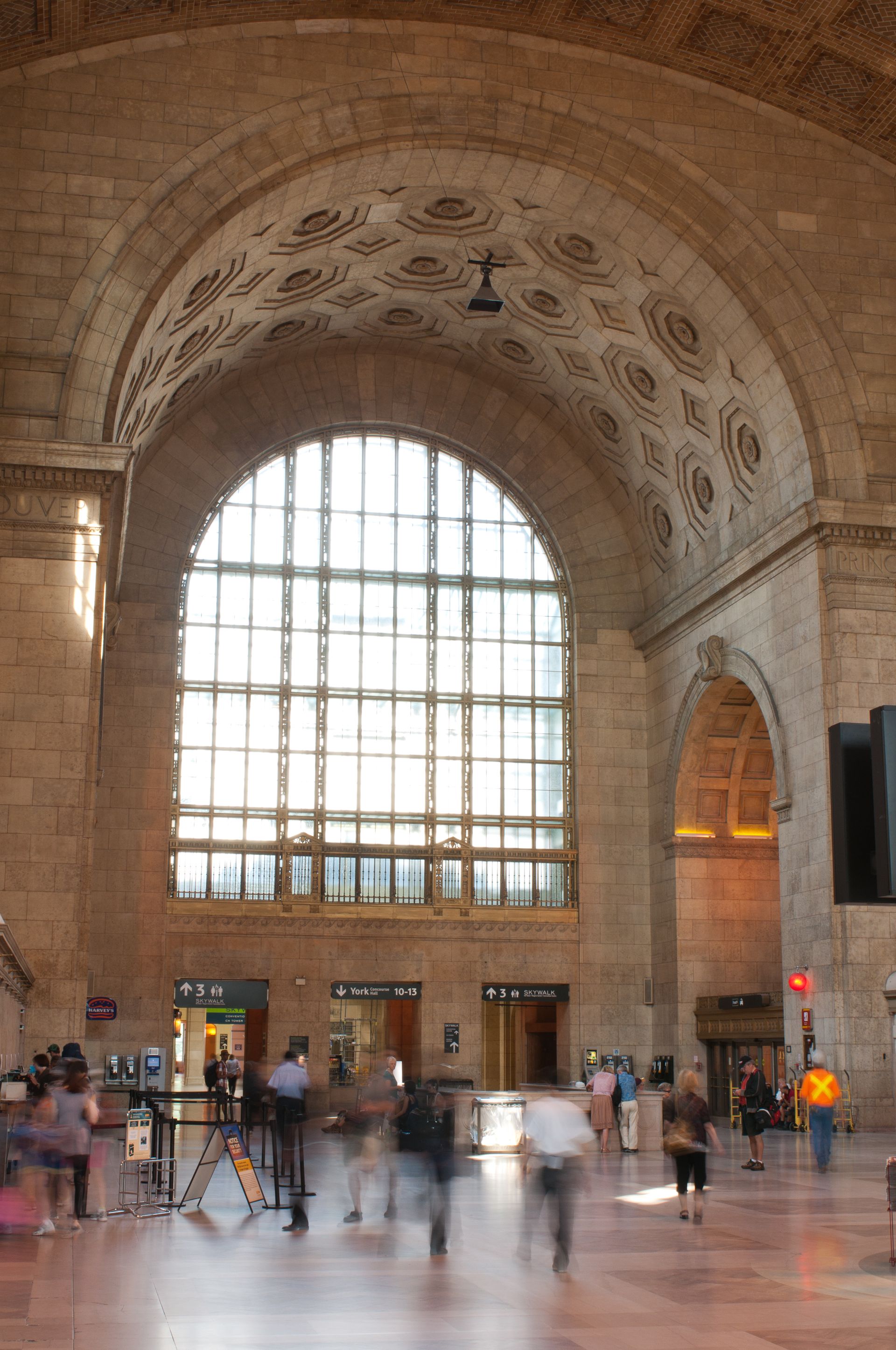Grand train station hall with a large arched window and blurred commuters on the floor