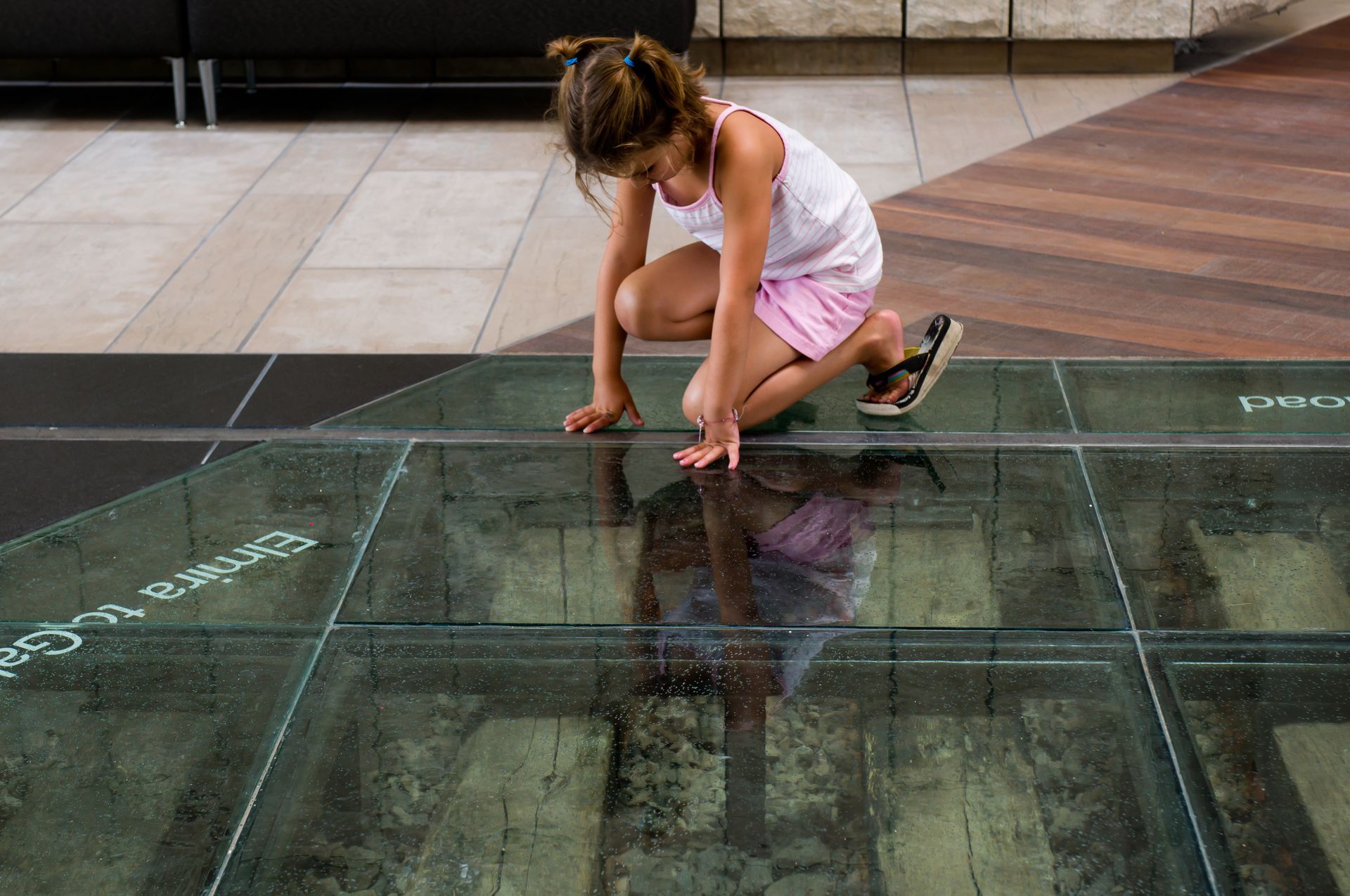 A young girl crouching on transparent glass flooring at a museum. A young girl crouching on transparent glass flooring at a museum.