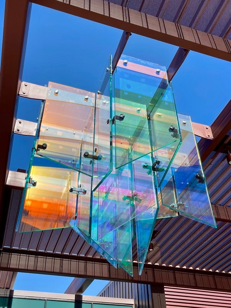 Colorful glass panels suspended in a modern wooden structure against a blue sky