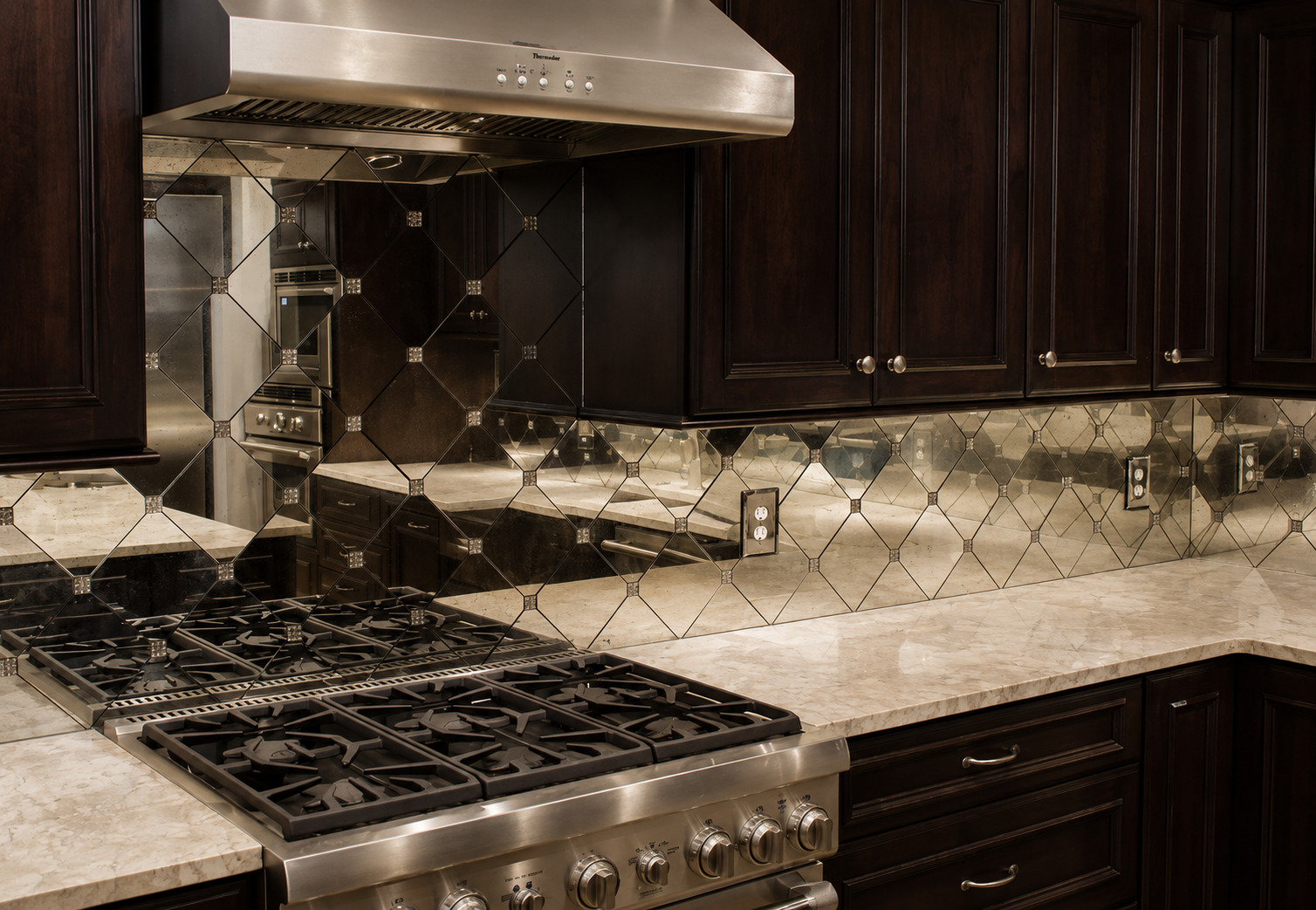Modern kitchen with dark cabinets, granite countertops, stainless-steel stove, range hood, and mirrored backsplash