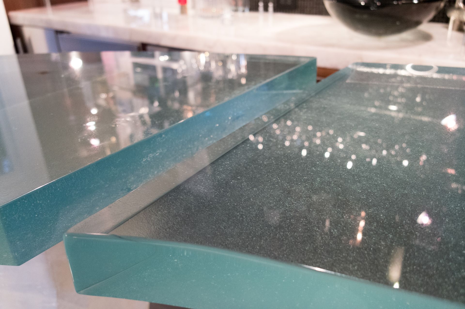 Close-up of two glass panes with teal edges on a reflective countertop.