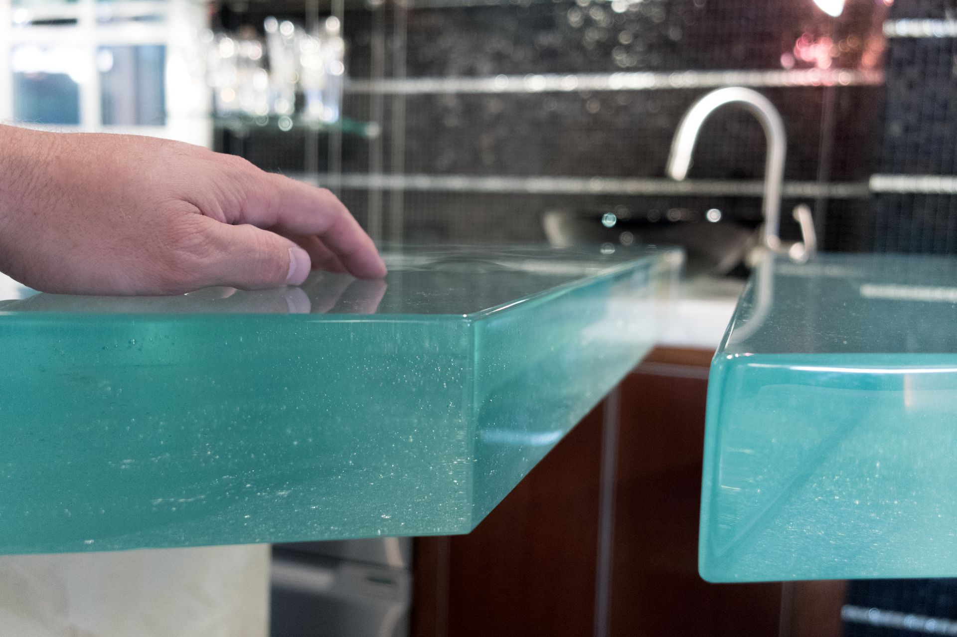 Hand hovering over a turquoise glass tabletop near a kitchen sink