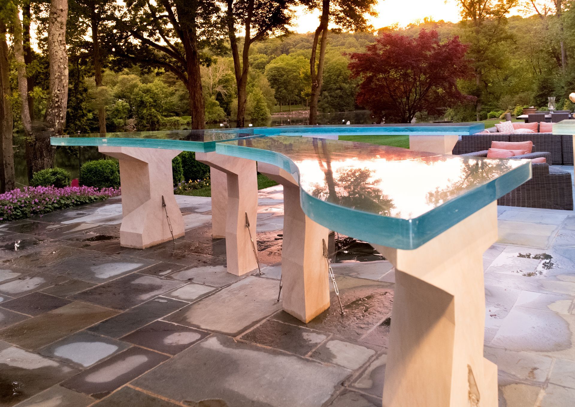 Outdoor stone dining table with turquoise edges on a patio, reflecting sunset light under trees