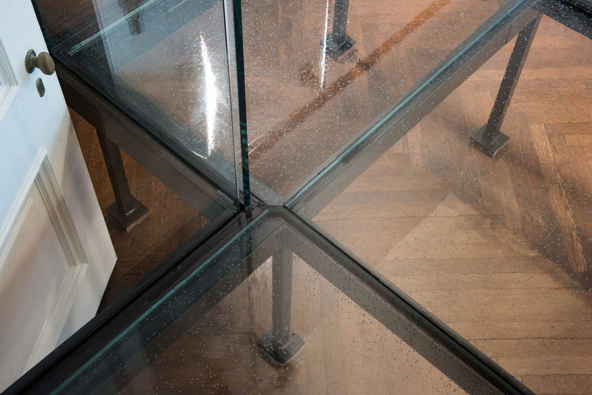 Glass-top table with black metal legs and reflective surfaces on a wooden floor