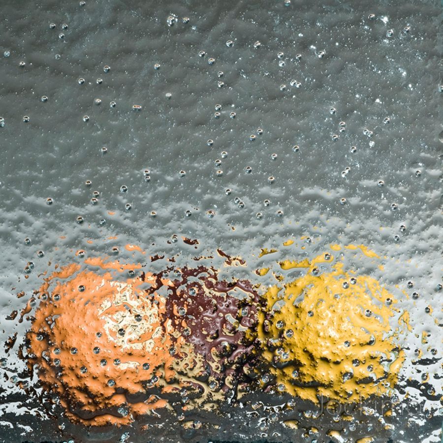 Two frosted pastries, one orange and one yellow, seen through rain-speckled glass