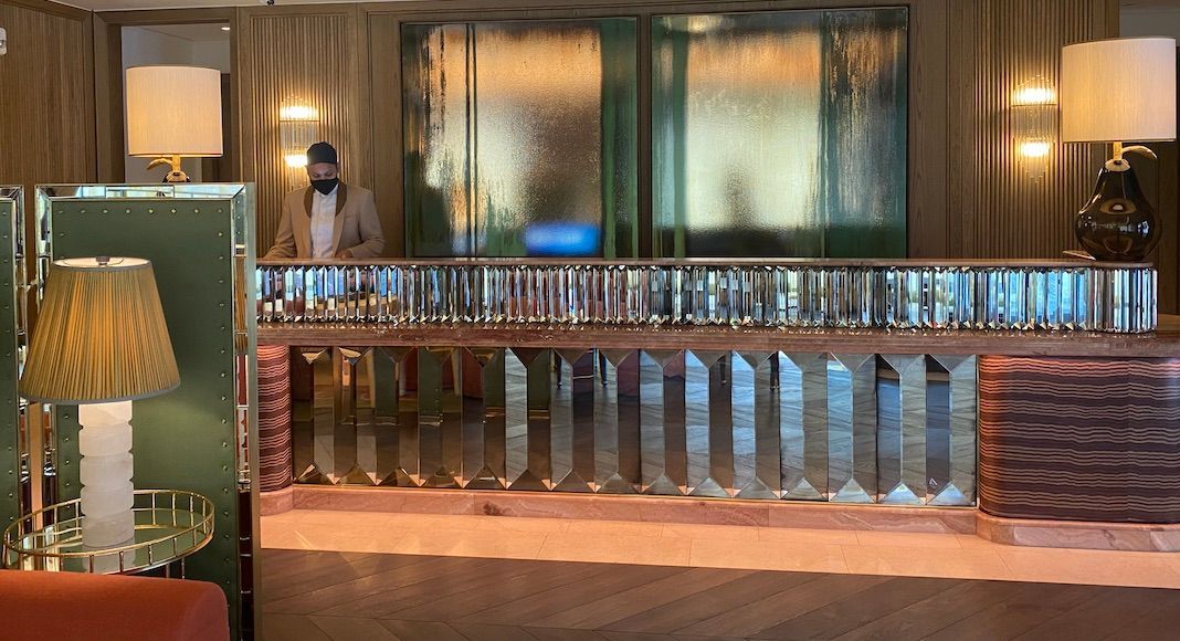 A man is standing behind a counter made of cast glass mouldings in a hotel lobby.