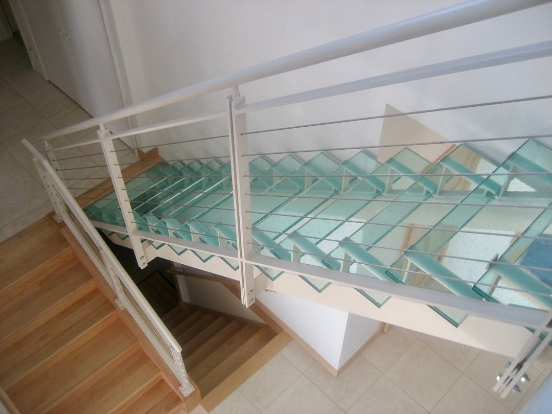 A staircase with wooden steps leading down to a lower level, alongside a flight of stairs featuring clear glass treads.
