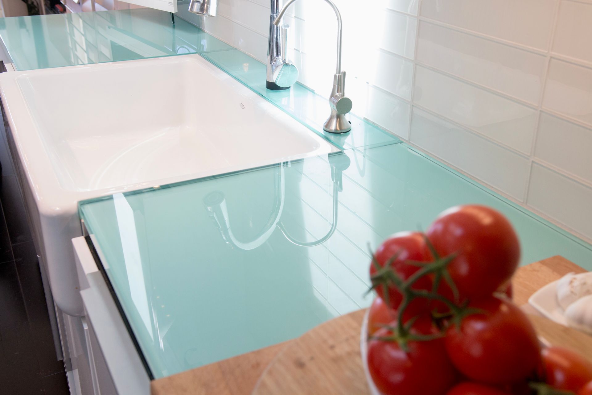 A bowl of tomatoes sits on a counter next to a sink.