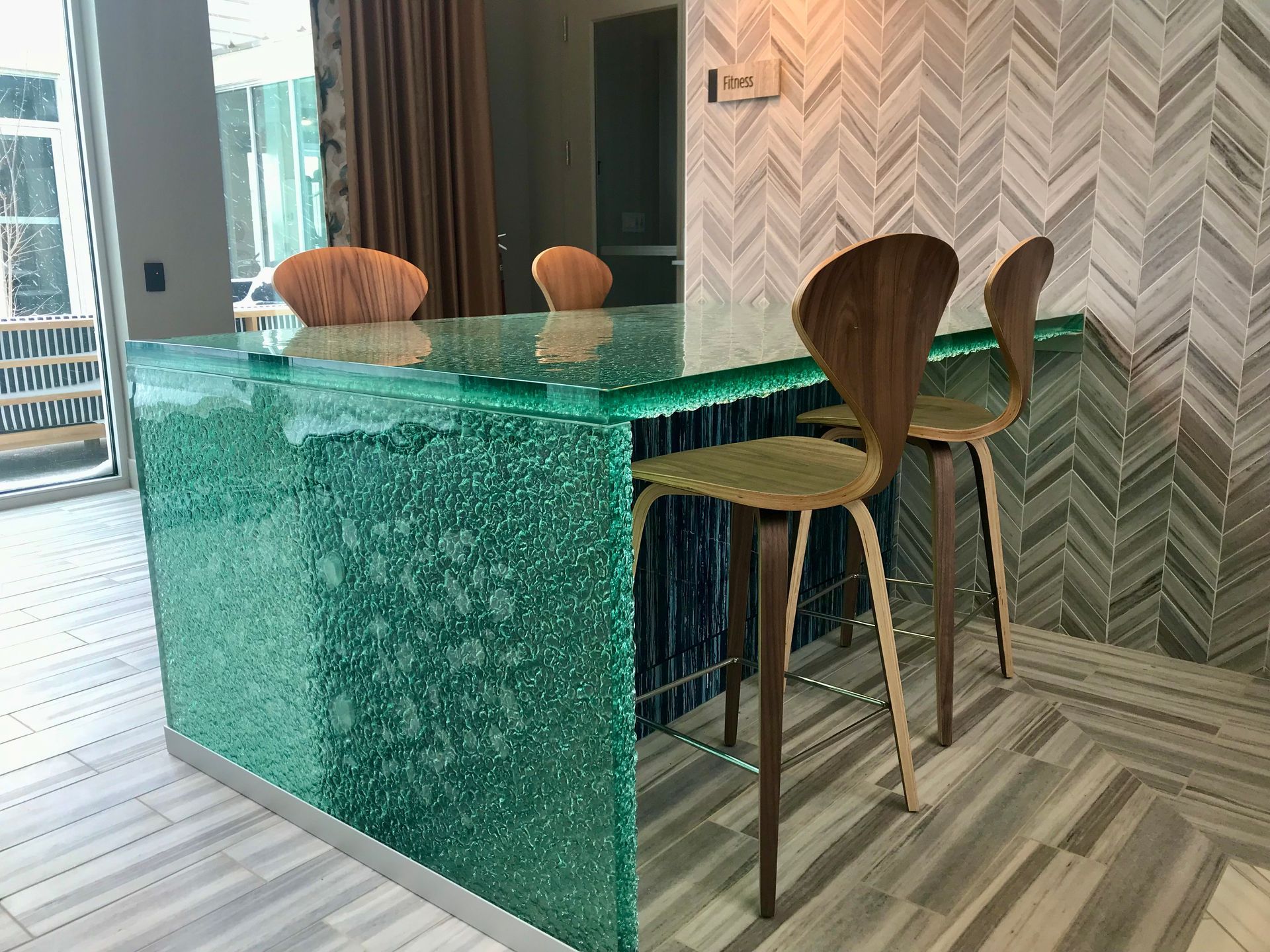 Turquoise glass kitchen island with wooden bar stools in a modern herringbone-tiled room