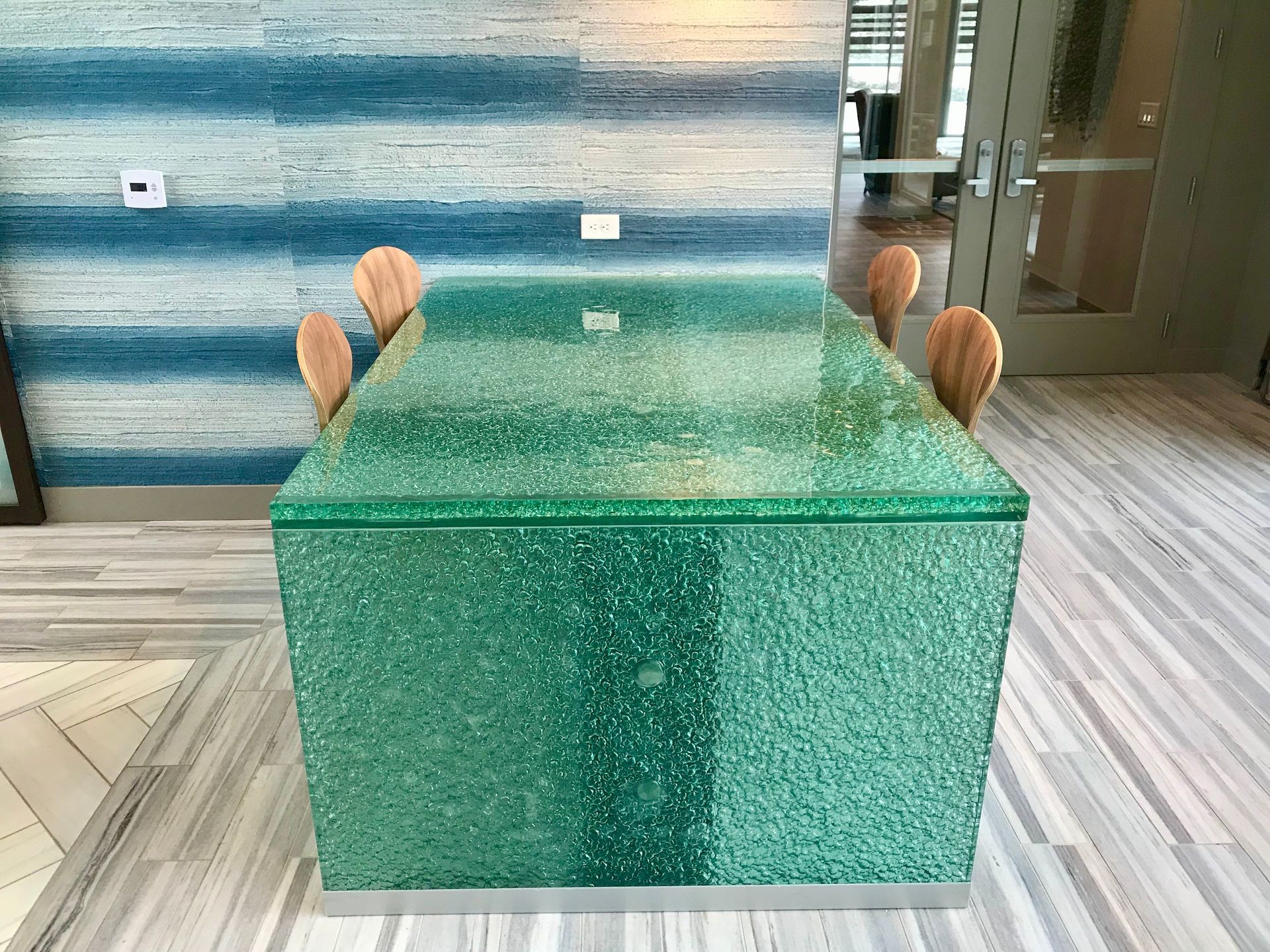 A green glass table with wooden chairs in a room.
