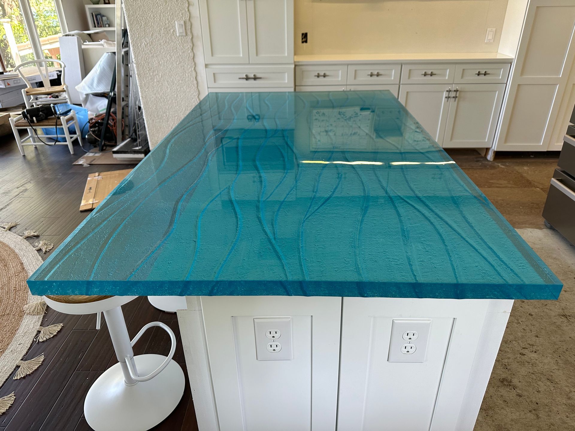A kitchen island with a blue thick glass counter top and white cabinets