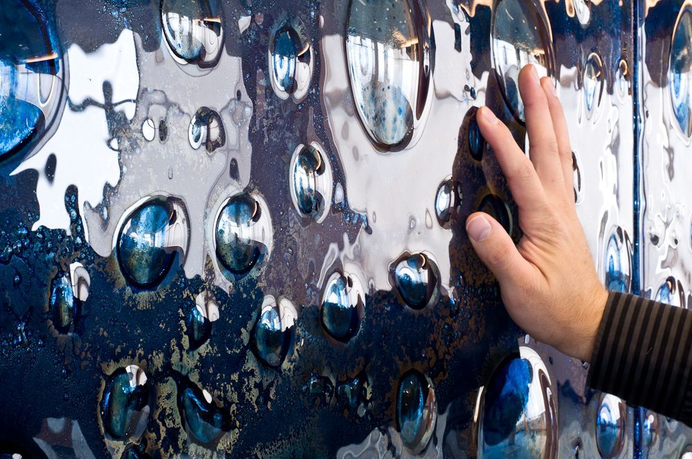 Hand touching a shiny blue, silver, and white textured metal surface