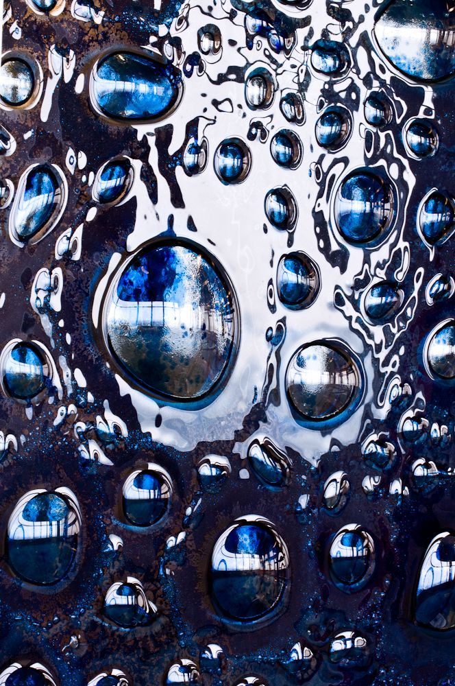 Close-up of water droplets on a dark surface with blue reflections