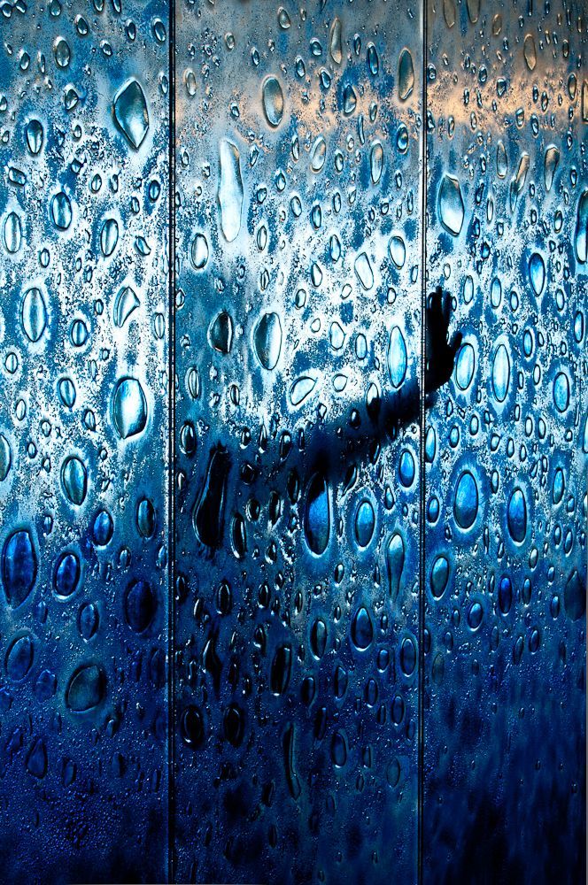 Silhouette of a person pressed against rain-covered blue glass panels
