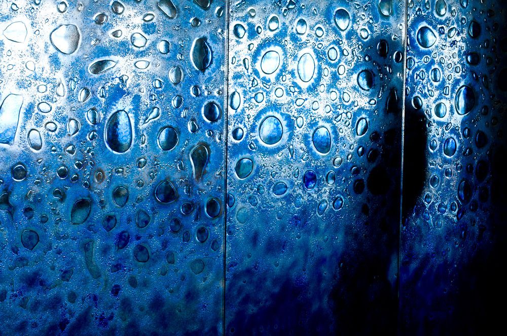 Blue raindrops and water droplets on a glass surface with dark shadows behind them