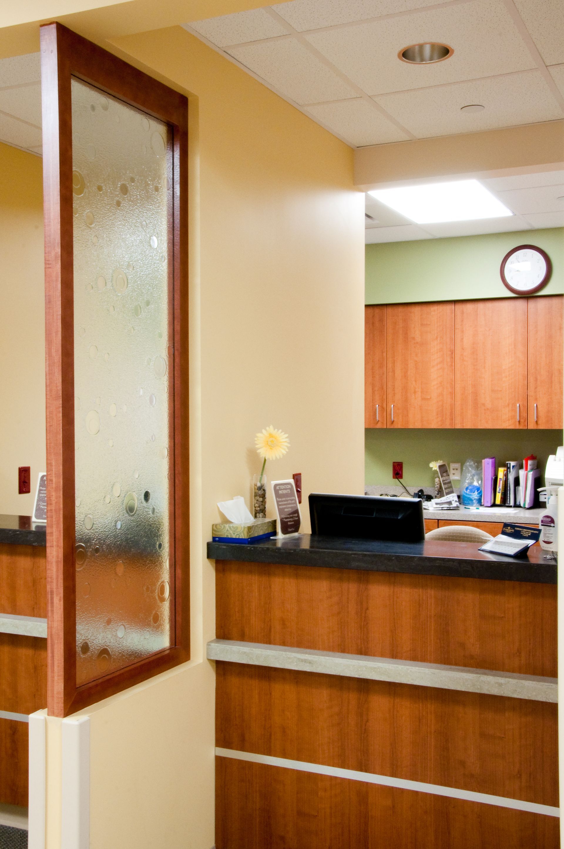 Reception desk in a beige office hallway with wood cabinets and a frosted glass door