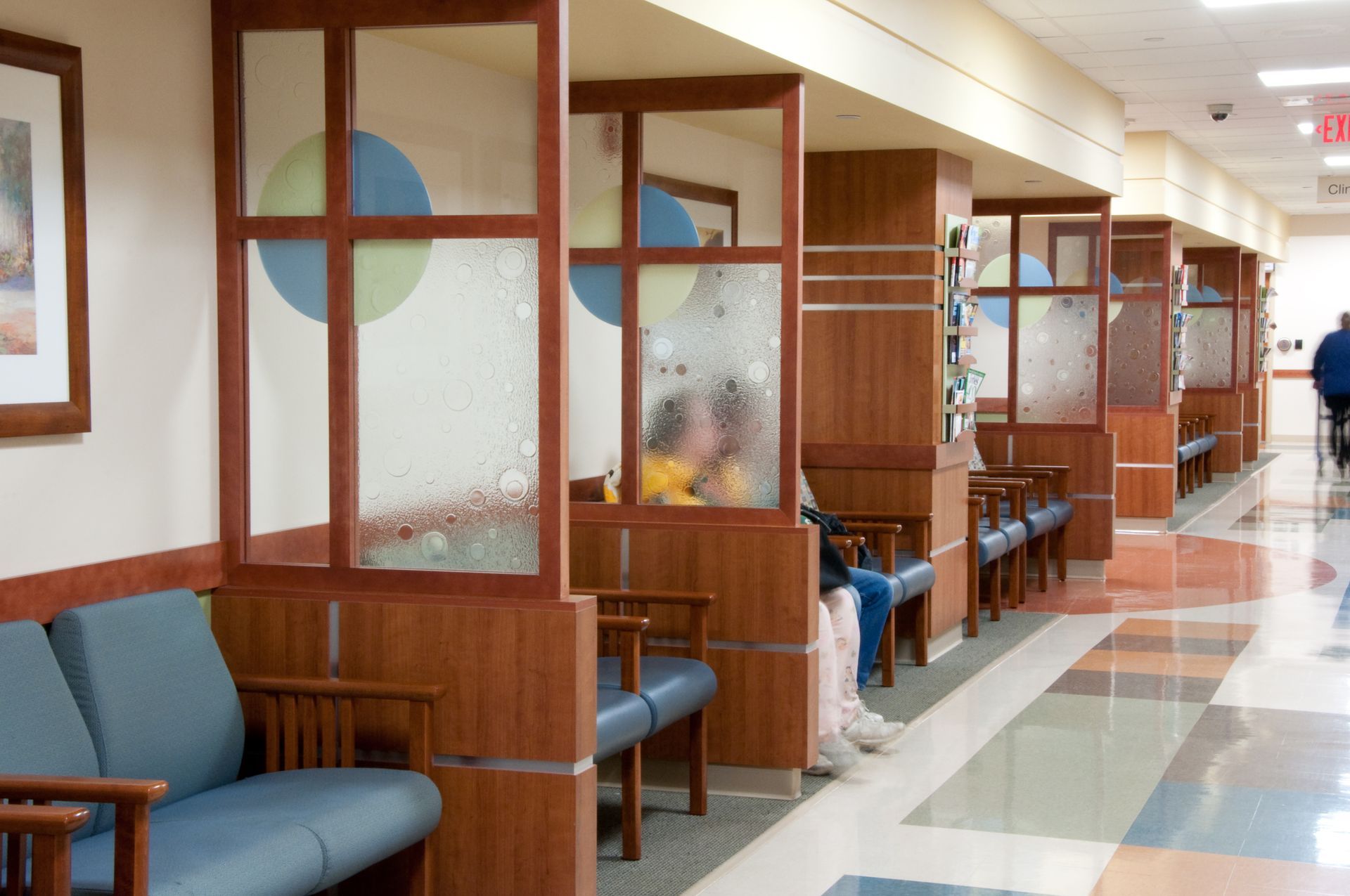 Empty hospital waiting area with blue chairs, wooden partitions, and polished hallway floor