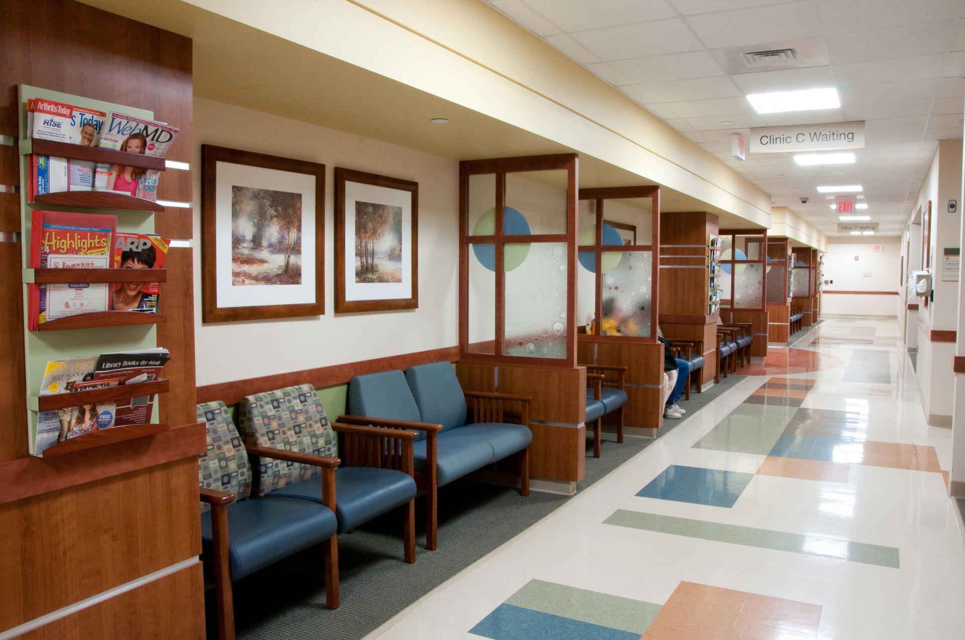 Empty hospital waiting hallway with chairs, framed art, and tiled floor