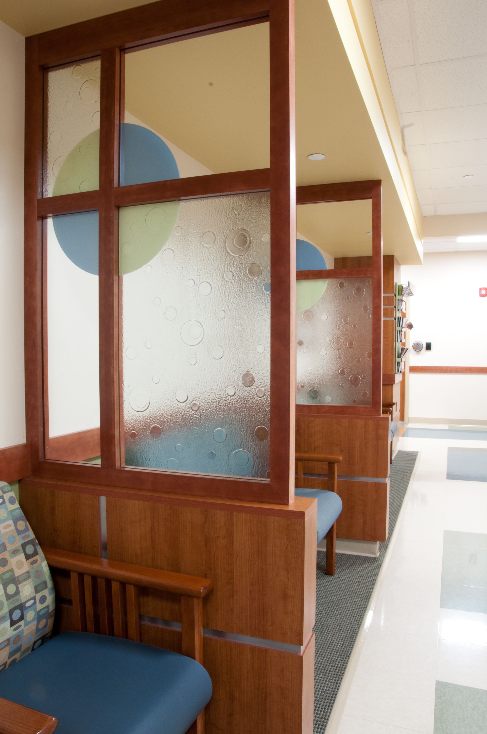 Empty hospital waiting area with blue chairs and wooden privacy booths with frosted glass panels