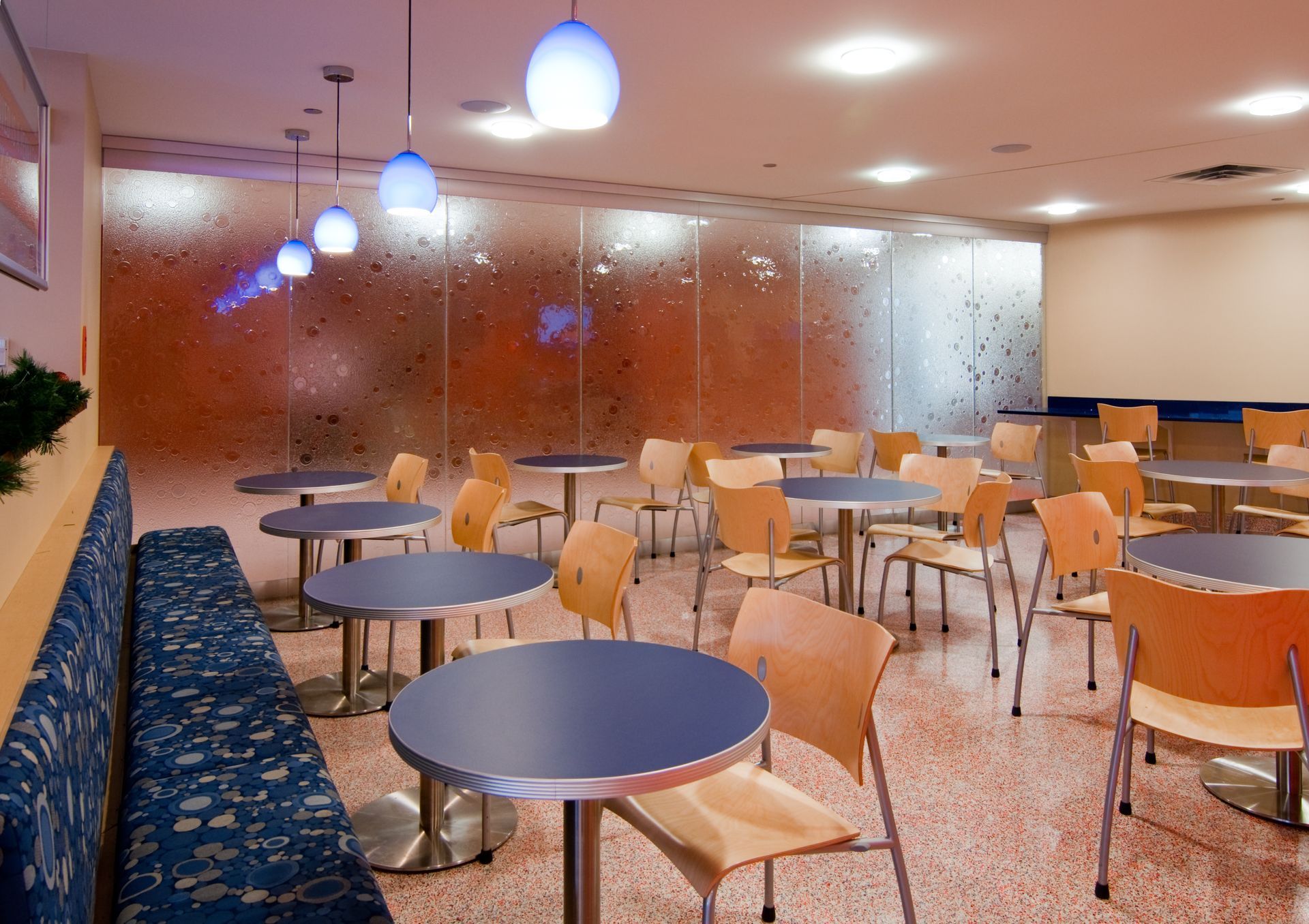 Empty modern café seating area with blue tables, wooden chairs, and hanging pendant lights.