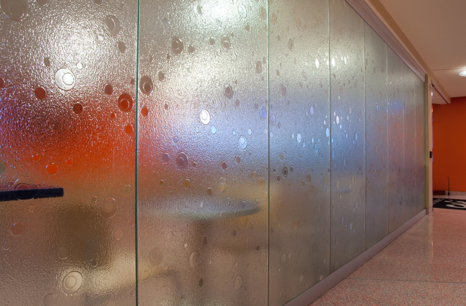 Colored frosted glass wall with blurred lights in a modern hallway and orange seating area