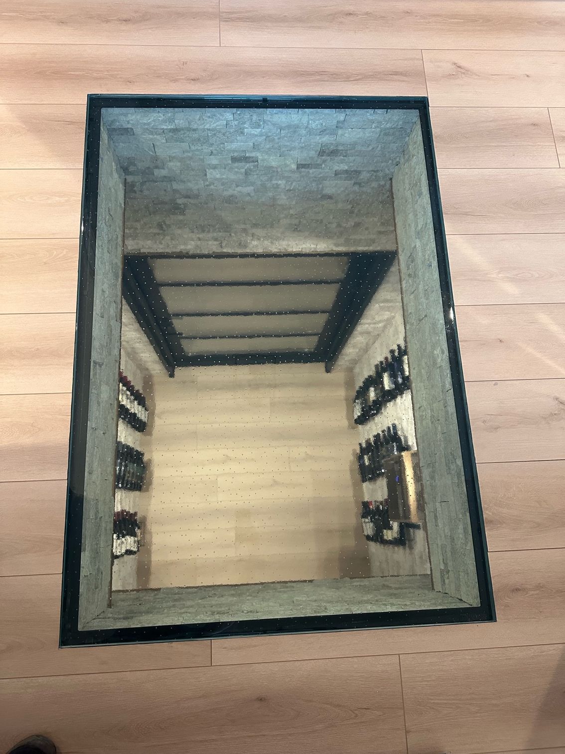 Glass floor panel reveals a small wine cellar with bottles on shelves.