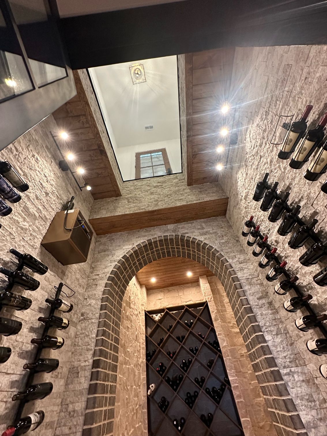 Wine cellar with brick walls and arched entry, bottles displayed on racks.