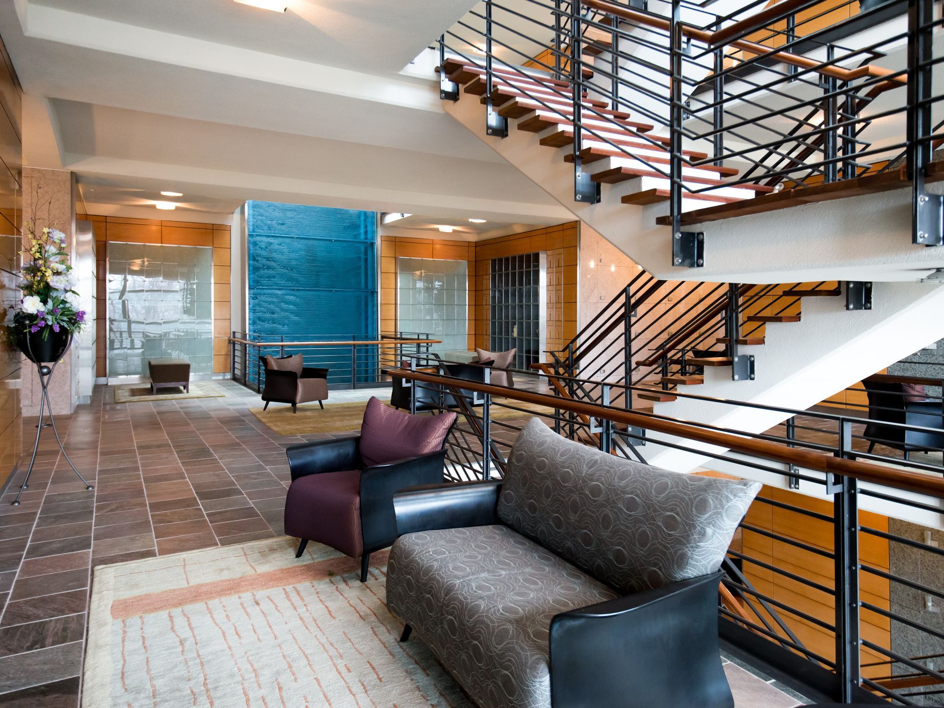 Modern hotel lobby with stairs, gray and purple seating, tiled floor, and a blue accent wall.