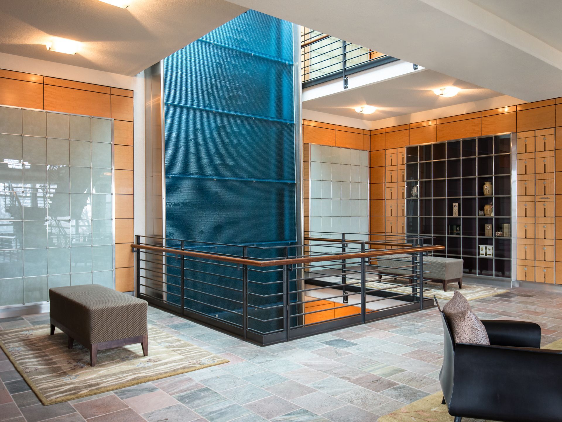 Modern lobby with blue central staircase, tiled floors, benches, and warm wood accents