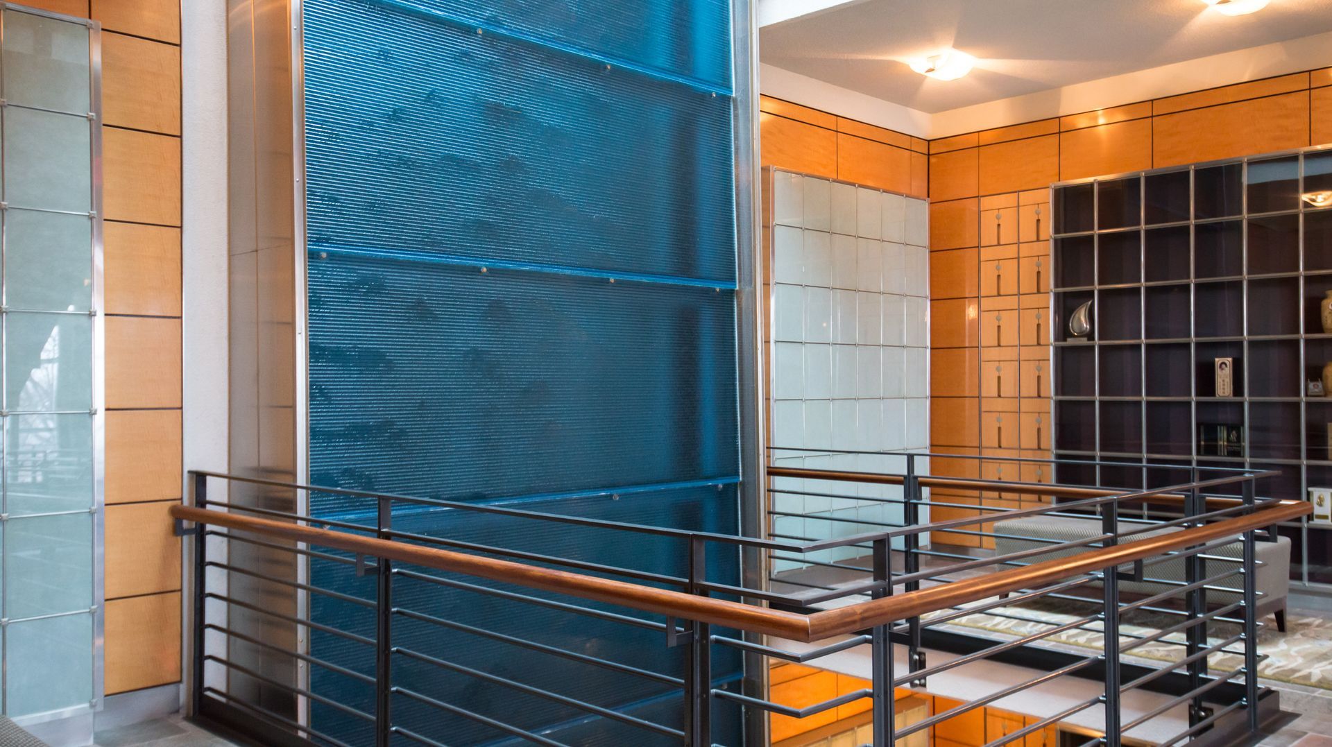 Modern interior with blue and orange tiled walls, metal railing, and a glass-block window wall
