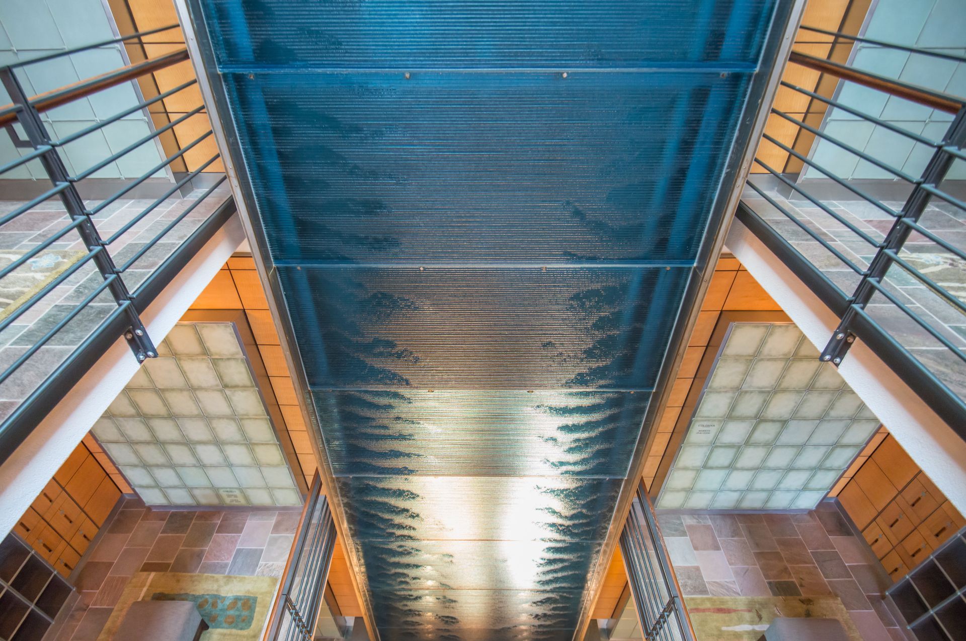 Symmetrical view up a modern atrium with blue glass ceiling and orange walls