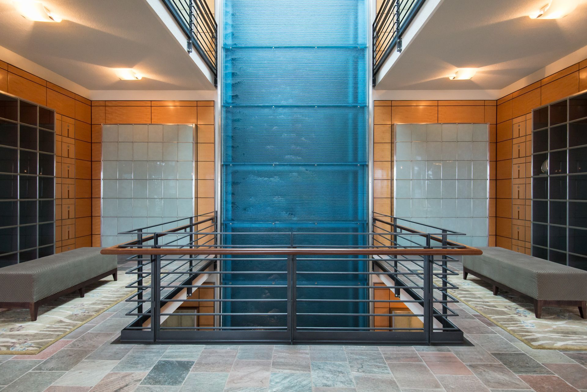 Symmetrical interior atrium with blue central staircase, glass railings, and warm-lit seating areas
