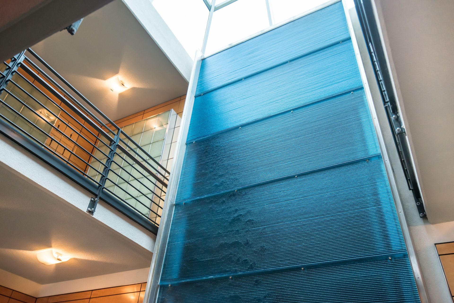 Interior atrium with a tall blue glass elevator and nearby balconies with railings